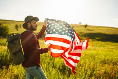 4 Temmuz. 4 Temmuz. Ulusal bayrağı olan Amerikalı. Amerikan bayrağı. Bağımsızlık günü. Vatanseverlik tatili. Adam şapka, sırt çantası, gömlek ve kot giyiyor. Güzel günbatımı ışık. 