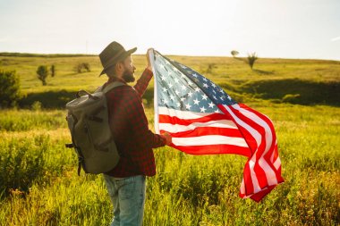 4 Temmuz. 4 Temmuz. Ulusal bayrağı olan Amerikalı. Amerikan bayrağı. Bağımsızlık günü. Vatanseverlik tatili. Adam şapka, sırt çantası, gömlek ve kot giyiyor. Güzel günbatımı ışık. 