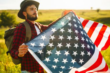 4 Temmuz. 4 Temmuz. Ulusal bayrağı olan Amerikalı. Amerikan bayrağı. Bağımsızlık günü. Vatanseverlik tatili. Adam şapka, sırt çantası, gömlek ve kot giyiyor. Güzel günbatımı ışık. 