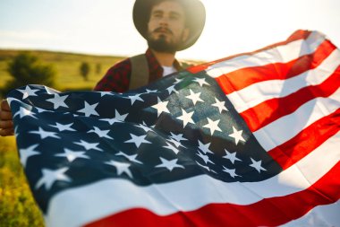 4 Temmuz. 4 Temmuz. Ulusal bayrağı olan Amerikalı. Amerikan bayrağı. Bağımsızlık günü. Vatanseverlik tatili. Adam şapka, sırt çantası, gömlek ve kot giyiyor. Güzel günbatımı ışık. 