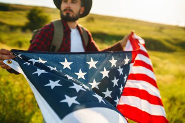 4 Temmuz. 4 Temmuz. Ulusal bayrağı olan Amerikalı. Amerikan bayrağı. Bağımsızlık günü. Vatanseverlik tatili. Adam şapka, sırt çantası, gömlek ve kot giyiyor. Güzel günbatımı ışık. 