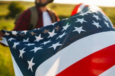 4 Temmuz. 4 Temmuz. Ulusal bayrağı olan Amerikalı. Amerikan bayrağı. Bağımsızlık günü. Vatanseverlik tatili. Adam şapka, sırt çantası, gömlek ve kot giyiyor. Güzel günbatımı ışık. 