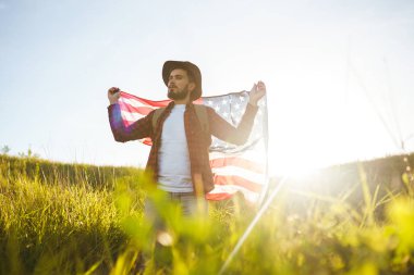 4 Temmuz. 4 Temmuz. Ulusal bayrağı olan Amerikalı. Amerikan bayrağı. Bağımsızlık günü. Vatanseverlik tatili. Adam şapka, sırt çantası, gömlek ve kot giyiyor. Güzel günbatımı ışık. 