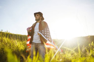 4 Temmuz. 4 Temmuz. Ulusal bayrağı olan Amerikalı. Amerikan bayrağı. Bağımsızlık günü. Vatanseverlik tatili. Adam şapka, sırt çantası, gömlek ve kot giyiyor. Güzel günbatımı ışık. 