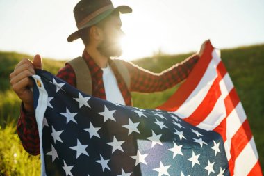 4 Temmuz. 4 Temmuz. Ulusal bayrağı olan Amerikalı. Amerikan bayrağı. Bağımsızlık günü. Vatanseverlik tatili. Adam şapka, sırt çantası, gömlek ve kot giyiyor. Güzel günbatımı ışık. 