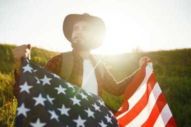 4 Temmuz. 4 Temmuz. Ulusal bayrağı olan Amerikalı. Amerikan bayrağı. Bağımsızlık günü. Vatanseverlik tatili. Adam şapka, sırt çantası, gömlek ve kot giyiyor. Güzel günbatımı ışık. 