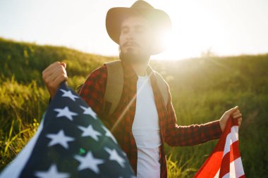 4 Temmuz. 4 Temmuz. Ulusal bayrağı olan Amerikalı. Amerikan bayrağı. Bağımsızlık günü. Vatanseverlik tatili. Adam şapka, sırt çantası, gömlek ve kot giyiyor. Güzel günbatımı ışık. 