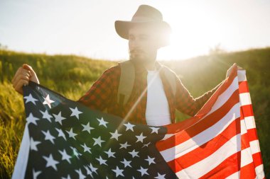 4 Temmuz. 4 Temmuz. Ulusal bayrağı olan Amerikalı. Amerikan bayrağı. Bağımsızlık günü. Vatanseverlik tatili. Adam şapka, sırt çantası, gömlek ve kot giyiyor. Güzel günbatımı ışık. 