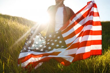 4 Temmuz. 4 Temmuz. Ulusal bayrağı olan Amerikalı. Amerikan bayrağı. Bağımsızlık günü. Vatanseverlik tatili. Adam şapka, sırt çantası, gömlek ve kot giyiyor. Güzel günbatımı ışık. 