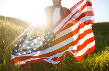 4 Temmuz. 4 Temmuz. Ulusal bayrağı olan Amerikalı. Amerikan bayrağı. Bağımsızlık günü. Vatanseverlik tatili. Adam şapka, sırt çantası, gömlek ve kot giyiyor. Güzel günbatımı ışık. 