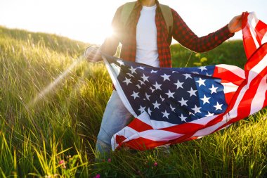 4 Temmuz. 4 Temmuz. Ulusal bayrağı olan Amerikalı. Amerikan bayrağı. Bağımsızlık günü. Vatanseverlik tatili. Adam şapka, sırt çantası, gömlek ve kot giyiyor. Güzel günbatımı ışık. 