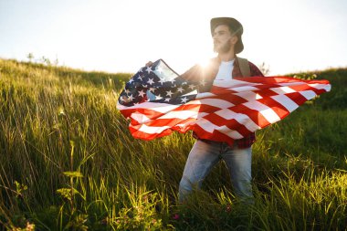 4 Temmuz. 4 Temmuz. Ulusal bayrağı olan Amerikalı. Amerikan bayrağı. Bağımsızlık günü. Vatanseverlik tatili. Adam şapka, sırt çantası, gömlek ve kot giyiyor. Güzel günbatımı ışık. 