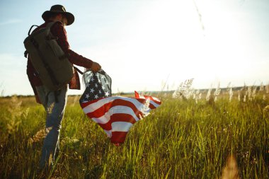 4 Temmuz. 4 Temmuz. Ulusal bayrağı olan Amerikalı. Amerikan bayrağı. Bağımsızlık günü. Vatanseverlik tatili. Adam şapka, sırt çantası, gömlek ve kot giyiyor. Güzel günbatımı ışık. 