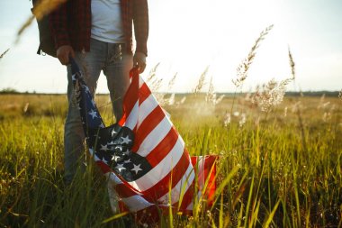 4 Temmuz. 4 Temmuz. Ulusal bayrağı olan Amerikalı. Amerikan bayrağı. Bağımsızlık günü. Vatanseverlik tatili. Adam şapka, sırt çantası, gömlek ve kot giyiyor. Güzel günbatımı ışık. 