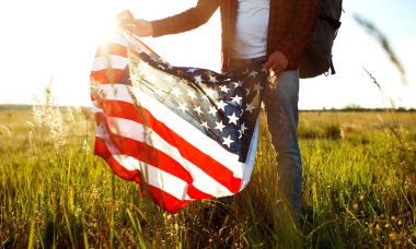 4 Temmuz. 4 Temmuz. Ulusal bayrağı olan Amerikalı. Amerikan bayrağı. Bağımsızlık günü. Vatanseverlik tatili. Adam şapka, sırt çantası, gömlek ve kot giyiyor. Güzel günbatımı ışık. 