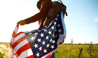 4 Temmuz. 4 Temmuz. Ulusal bayrağı olan Amerikalı. Amerikan bayrağı. Bağımsızlık günü. Vatanseverlik tatili. Adam şapka, sırt çantası, gömlek ve kot giyiyor. Güzel günbatımı ışık. 