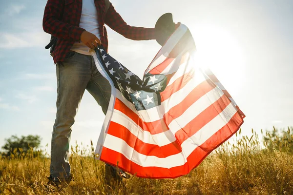 4 Temmuz. 4 Temmuz. Ulusal bayrağı olan Amerikalı. Amerikan bayrağı. Bağımsızlık günü. Vatanseverlik tatili. Adam şapka, sırt çantası, gömlek ve kot giyiyor. Güzel günbatımı ışık. 