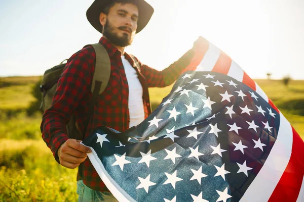 4 Temmuz. 4 Temmuz. Ulusal bayrağı olan Amerikalı. Amerikan bayrağı. Bağımsızlık günü. Vatanseverlik tatili. Adam şapka, sırt çantası, gömlek ve kot giyiyor. Güzel günbatımı ışık. 