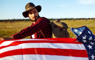 4 Temmuz. 4 Temmuz. Ulusal bayrağı olan Amerikalı. Amerikan bayrağı. Bağımsızlık günü. Vatanseverlik tatili. Adam şapka, sırt çantası, gömlek ve kot giyiyor. Güzel günbatımı ışık. 