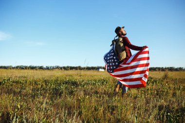 4 Temmuz. 4 Temmuz. Ulusal bayrağı olan Amerikalı. Amerikan bayrağı. Bağımsızlık günü. Vatanseverlik tatili. Adam şapka, sırt çantası, gömlek ve kot giyiyor. Güzel günbatımı ışık. 