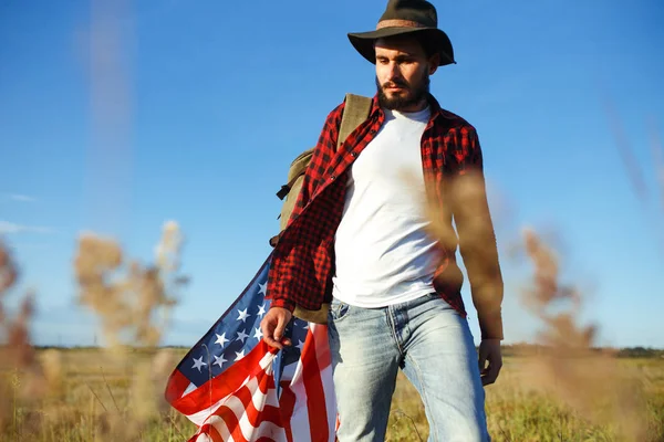 4 Temmuz. 4 Temmuz. Ulusal bayrağı olan Amerikalı. Amerikan bayrağı. Bağımsızlık günü. Vatanseverlik tatili. Adam şapka, sırt çantası, gömlek ve kot giyiyor. Güzel günbatımı ışık. 