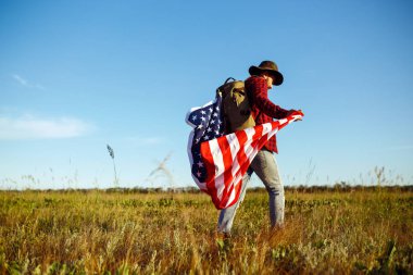 4 Temmuz. 4 Temmuz. Ulusal bayrağı olan Amerikalı. Amerikan bayrağı. Bağımsızlık günü. Vatanseverlik tatili. Adam şapka, sırt çantası, gömlek ve kot giyiyor. Güzel günbatımı ışık. 