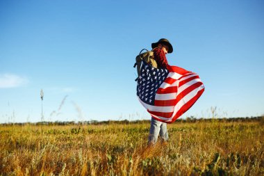 4 Temmuz. 4 Temmuz. Ulusal bayrağı olan Amerikalı. Amerikan bayrağı. Bağımsızlık günü. Vatanseverlik tatili. Adam şapka, sırt çantası, gömlek ve kot giyiyor. Güzel günbatımı ışık. 