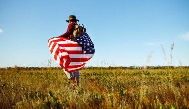 4 Temmuz. 4 Temmuz. Ulusal bayrağı olan Amerikalı. Amerikan bayrağı. Bağımsızlık günü. Vatanseverlik tatili. Adam şapka, sırt çantası, gömlek ve kot giyiyor. Güzel günbatımı ışık. 