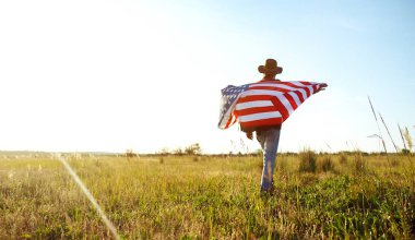 4 Temmuz. 4 Temmuz. Ulusal bayrağı olan Amerikalı. Amerikan bayrağı. Bağımsızlık günü. Vatanseverlik tatili. Adam şapka, sırt çantası, gömlek ve kot giyiyor. Güzel günbatımı ışık. 