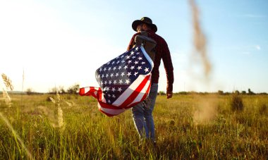 4 Temmuz. 4 Temmuz. Ulusal bayrağı olan Amerikalı. Amerikan bayrağı. Bağımsızlık günü. Vatanseverlik tatili. Adam şapka, sırt çantası, gömlek ve kot giyiyor. Güzel günbatımı ışık. 
