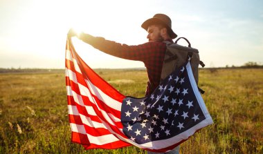 4 Temmuz. 4 Temmuz. Ulusal bayrağı olan Amerikalı. Amerikan bayrağı. Bağımsızlık günü. Vatanseverlik tatili. Adam şapka, sırt çantası, gömlek ve kot giyiyor. Güzel günbatımı ışık. 