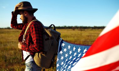 4 Temmuz. 4 Temmuz. Ulusal bayrağı olan Amerikalı. Amerikan bayrağı. Bağımsızlık günü. Vatanseverlik tatili. Adam şapka, sırt çantası, gömlek ve kot giyiyor. Güzel günbatımı ışık. 