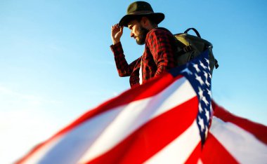 4 Temmuz. 4 Temmuz. Ulusal bayrağı olan Amerikalı. Amerikan bayrağı. Bağımsızlık günü. Vatanseverlik tatili. Adam şapka, sırt çantası, gömlek ve kot giyiyor. Güzel günbatımı ışık. 