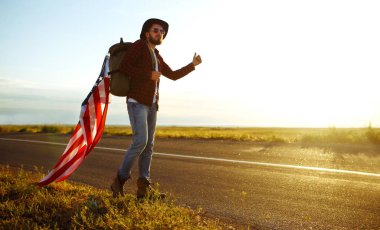 4 Temmuz. 4 Temmuz. Ulusal bayrağı olan Amerikalı. Amerikan bayrağı. Bağımsızlık günü. Vatanseverlik tatili. Adam şapka, sırt çantası, gömlek ve kot giyiyor. Güzel günbatımı ışık. 