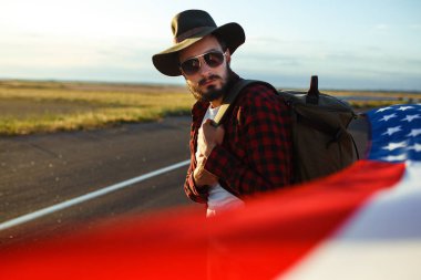 4 Temmuz. 4 Temmuz. Ulusal bayrağı olan Amerikalı. Amerikan bayrağı. Bağımsızlık günü. Vatanseverlik tatili. Adam şapka, sırt çantası, gömlek ve kot giyiyor. Güzel günbatımı ışık. 