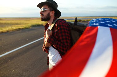 4 Temmuz. 4 Temmuz. Ulusal bayrağı olan Amerikalı. Amerikan bayrağı. Bağımsızlık günü. Vatanseverlik tatili. Adam şapka, sırt çantası, gömlek ve kot giyiyor. Güzel günbatımı ışık. 