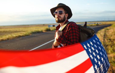 4 Temmuz. 4 Temmuz. Ulusal bayrağı olan Amerikalı. Amerikan bayrağı. Bağımsızlık günü. Vatanseverlik tatili. Adam şapka, sırt çantası, gömlek ve kot giyiyor. Güzel günbatımı ışık. 