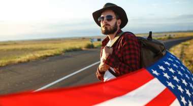 4 Temmuz. 4 Temmuz. Ulusal bayrağı olan Amerikalı. Amerikan bayrağı. Bağımsızlık günü. Vatanseverlik tatili. Adam şapka, sırt çantası, gömlek ve kot giyiyor. Güzel günbatımı ışık. 