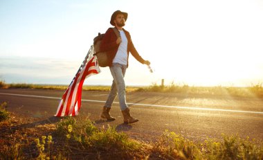 4 Temmuz. 4 Temmuz. Ulusal bayrağı olan Amerikalı. Amerikan bayrağı. Bağımsızlık günü. Vatanseverlik tatili. Adam şapka, sırt çantası, gömlek ve kot giyiyor. Güzel günbatımı ışık. 