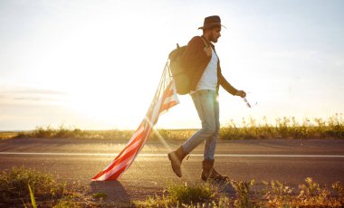 4 Temmuz. 4 Temmuz. Ulusal bayrağı olan Amerikalı. Amerikan bayrağı. Bağımsızlık günü. Vatanseverlik tatili. Adam şapka, sırt çantası, gömlek ve kot giyiyor. Güzel günbatımı ışık. 