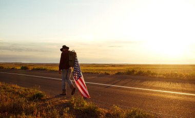 4 Temmuz. 4 Temmuz. Ulusal bayrağı olan Amerikalı. Amerikan bayrağı. Bağımsızlık günü. Vatanseverlik tatili. Adam şapka, sırt çantası, gömlek ve kot giyiyor. Güzel günbatımı ışık. 