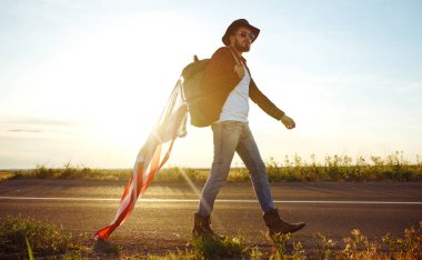 4 Temmuz. 4 Temmuz. Ulusal bayrağı olan Amerikalı. Amerikan bayrağı. Bağımsızlık günü. Vatanseverlik tatili. Adam şapka, sırt çantası, gömlek ve kot giyiyor. Güzel günbatımı ışık. 