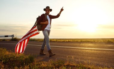 4 Temmuz. 4 Temmuz. Ulusal bayrağı olan Amerikalı. Amerikan bayrağı. Bağımsızlık günü. Vatanseverlik tatili. Adam şapka, sırt çantası, gömlek ve kot giyiyor. Güzel günbatımı ışık. 
