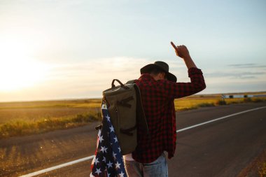 4 Temmuz. 4 Temmuz. Ulusal bayrağı olan Amerikalı. Amerikan bayrağı. Bağımsızlık günü. Vatanseverlik tatili. Adam şapka, sırt çantası, gömlek ve kot giyiyor. Güzel günbatımı ışık. 