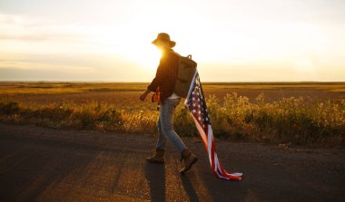 4 Temmuz. 4 Temmuz. Ulusal bayrağı olan Amerikalı. Amerikan bayrağı. Bağımsızlık günü. Vatanseverlik tatili. Adam şapka, sırt çantası, gömlek ve kot giyiyor. Güzel günbatımı ışık. 