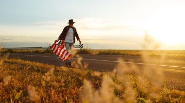 4 Temmuz. 4 Temmuz. Ulusal bayrağı olan Amerikalı. Amerikan bayrağı. Bağımsızlık günü. Vatanseverlik tatili. Adam şapka, sırt çantası, gömlek ve kot giyiyor. Güzel günbatımı ışık. 