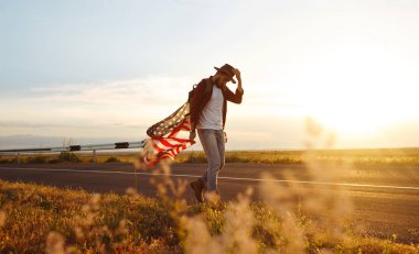 4 Temmuz. 4 Temmuz. Ulusal bayrağı olan Amerikalı. Amerikan bayrağı. Bağımsızlık günü. Vatanseverlik tatili. Adam şapka, sırt çantası, gömlek ve kot giyiyor. Güzel günbatımı ışık. 