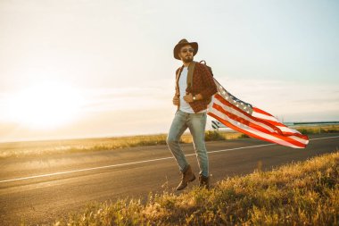 4 Temmuz. 4 Temmuz. Ulusal bayrağı olan Amerikalı. Amerikan bayrağı. Bağımsızlık günü. Vatanseverlik tatili. Adam şapka, sırt çantası, gömlek ve kot giyiyor. Güzel günbatımı ışık. 