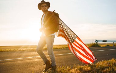 4 Temmuz. 4 Temmuz. Ulusal bayrağı olan Amerikalı. Amerikan bayrağı. Bağımsızlık günü. Vatanseverlik tatili. Adam şapka, sırt çantası, gömlek ve kot giyiyor. Güzel günbatımı ışık. 