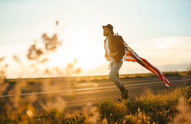 4 Temmuz. 4 Temmuz. Ulusal bayrağı olan Amerikalı. Amerikan bayrağı. Bağımsızlık günü. Vatanseverlik tatili. Adam şapka, sırt çantası, gömlek ve kot giyiyor. Güzel günbatımı ışık. 